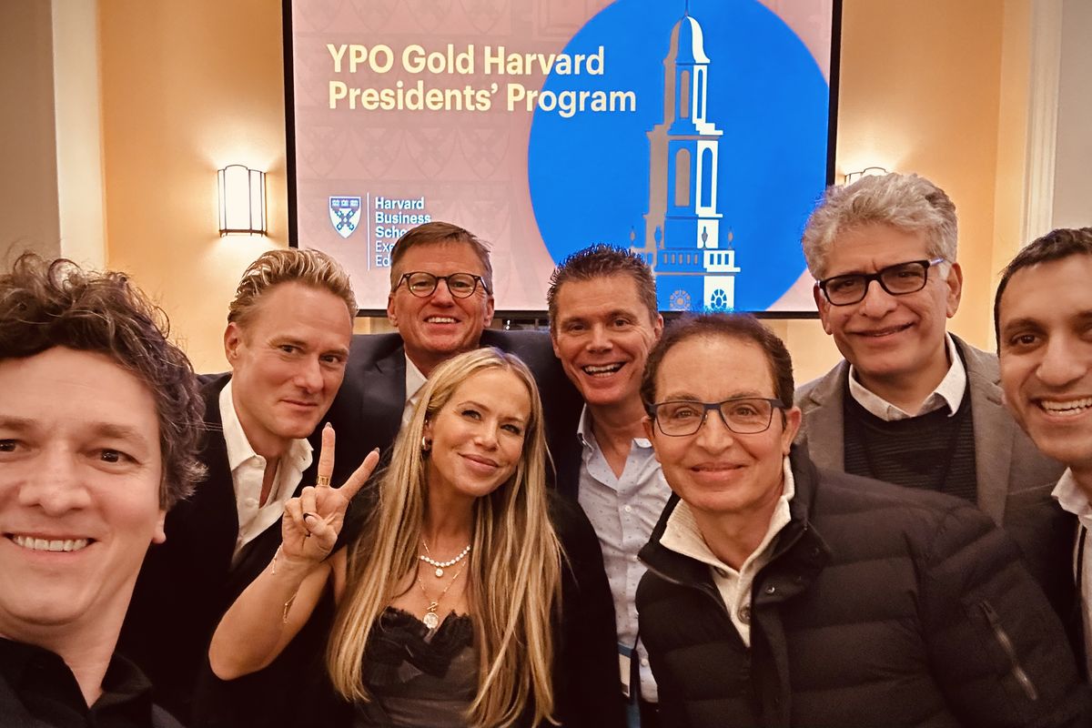 A group photographed in front of a screen reading YPO Gold Harvard Presidents' Program, the Harvard Business School shield beside it