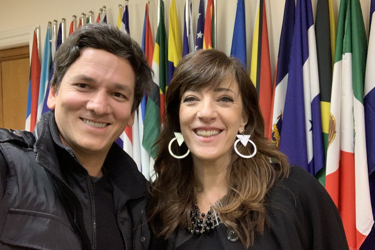 Two people in front of a row of national flags