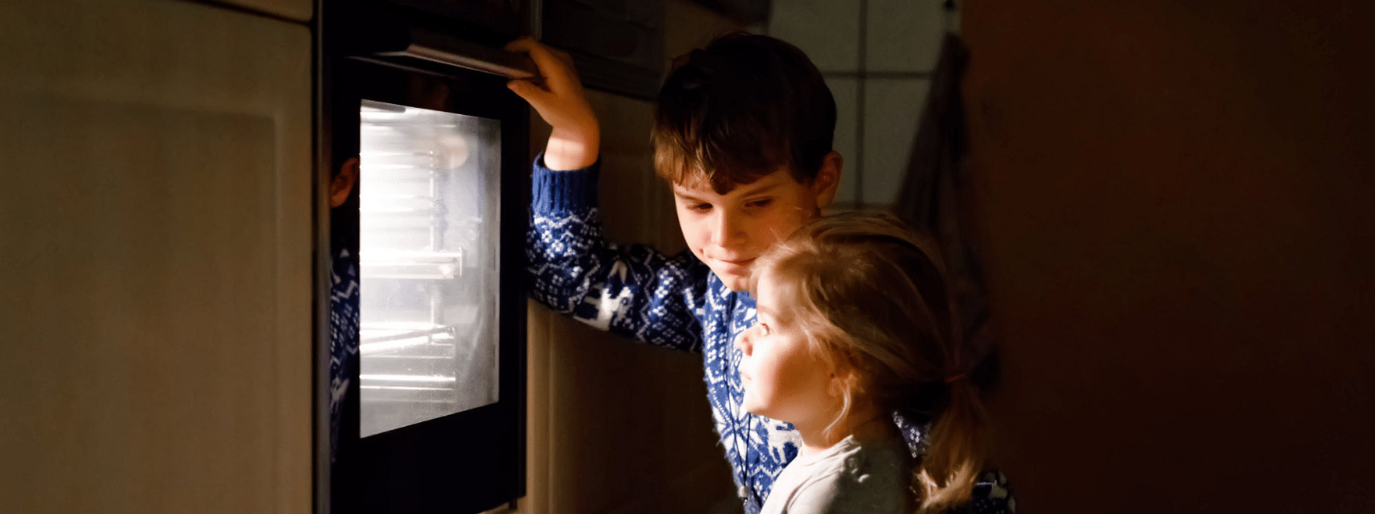 Two children at the oven, waiting on a tray of cookies